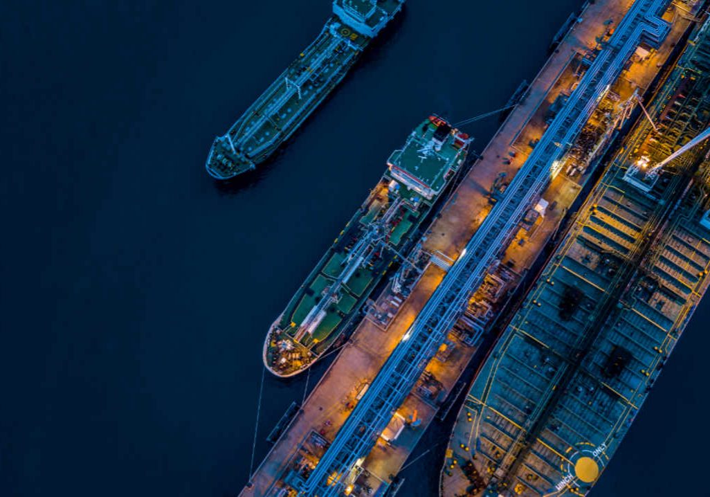 Aerial view Crude oil tanker under cargo operations on typical shore station with clearly visible mechanical loading arms and pipeline infrastructure.